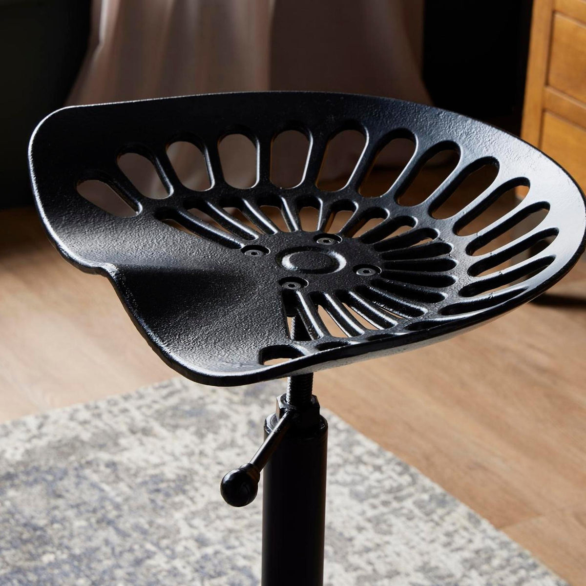 Black metal chair seat with adjustable height on a wooden floor.