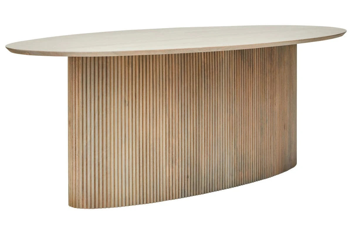 The Hawthorn Grey Mango Wood Oval Dining Table from a three-quarter angle, showing the oval top and reeded pedestal base in a washed grey finish.