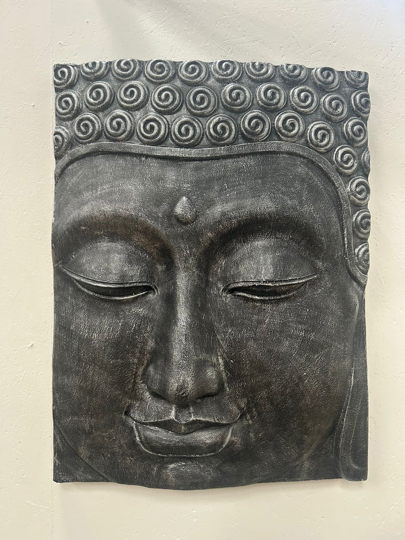 Decorative wall art of a Buddha face with a textured finish on a plain background
