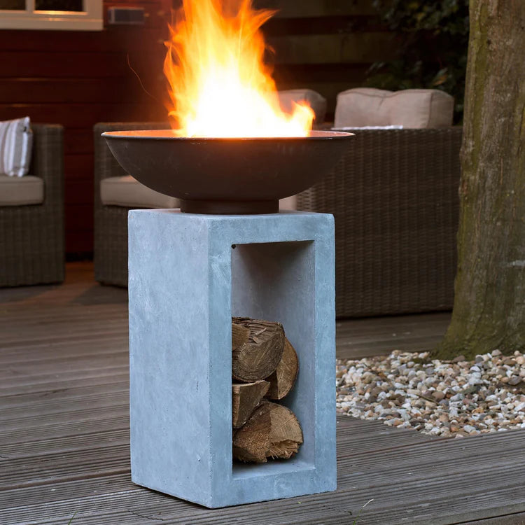 Fire pit with burning fire on a wooden deck with chairs and a tree in the background