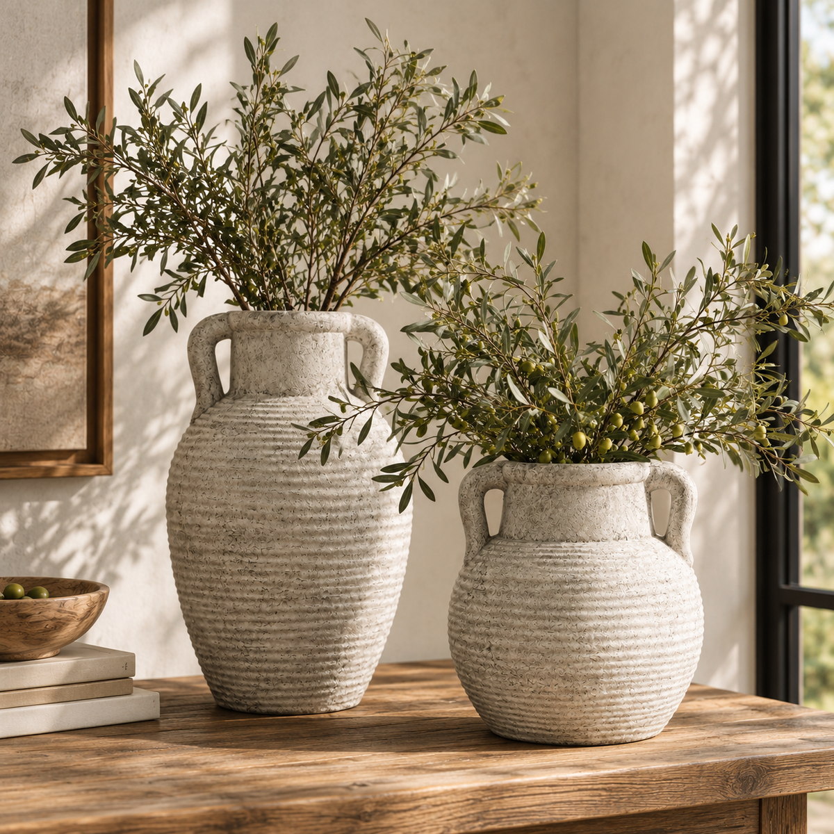 Two Athena Amphora Pots in different sizes holding olive branches on a wooden sideboard by a window