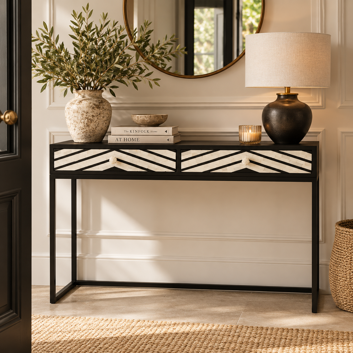 A black metal console table with white chevron-patterned drawer fronts, styled in a bright entryway with a vase of greenery, books, a lamp, and a candle.