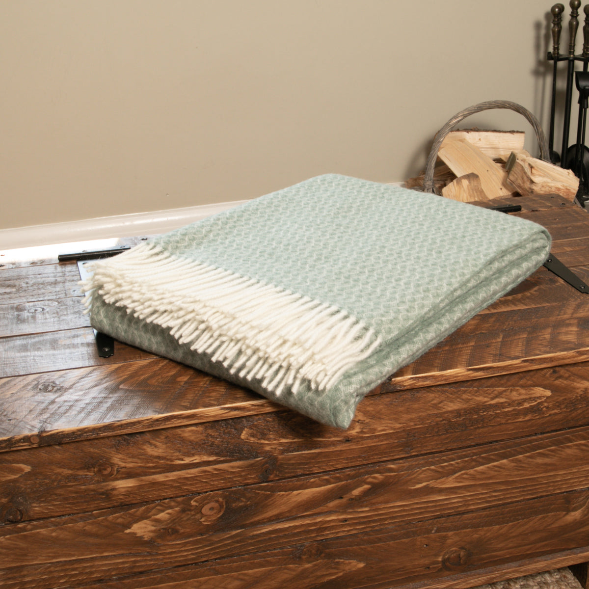 Hoop Pattern Green Wool Blanket folded on a wooden chest beside a log basket