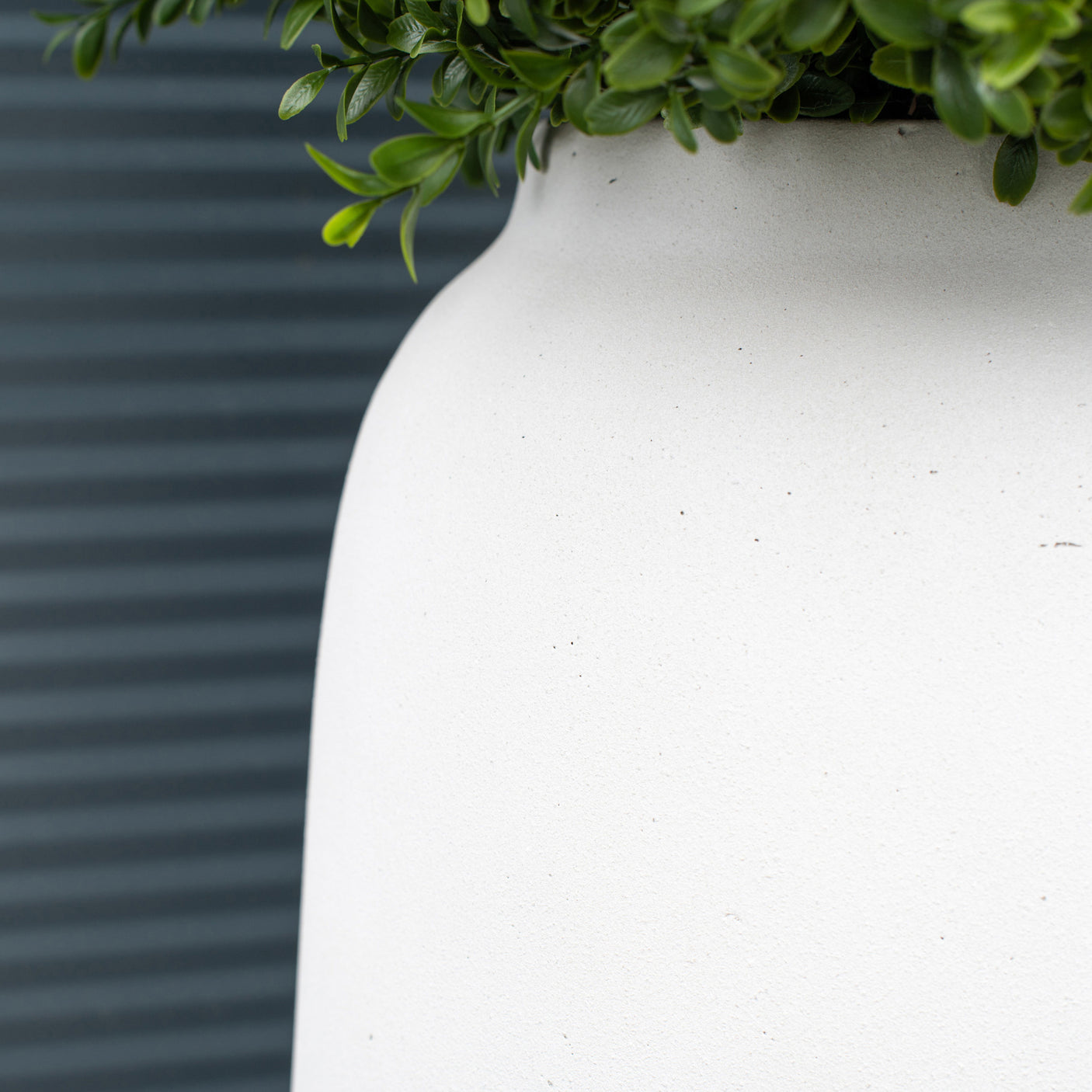 A close up of a textured off-white outdoor planter against a textured green background