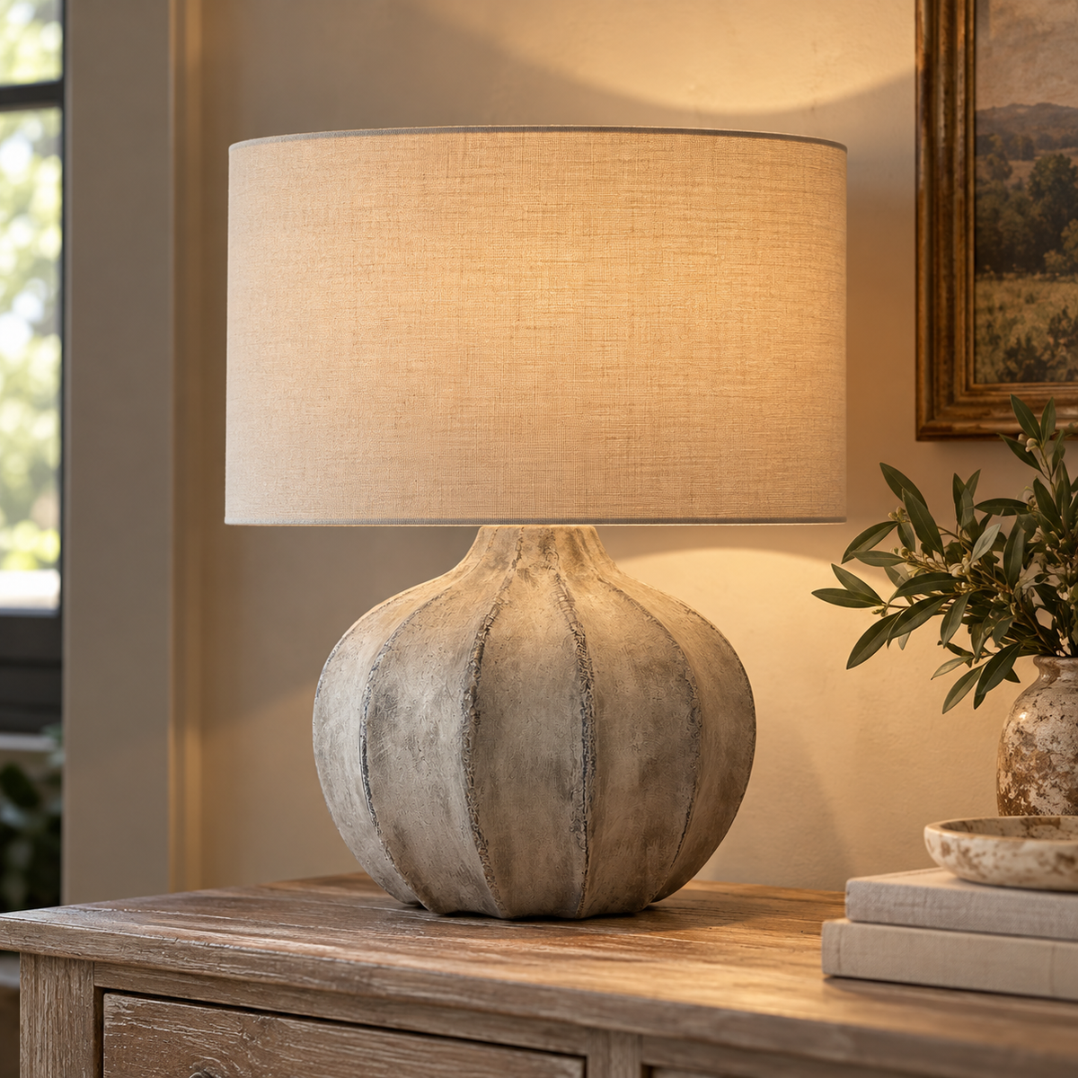 Darcy Antique White Flute Table Lamp lit on a wooden chest beside olive branches and books