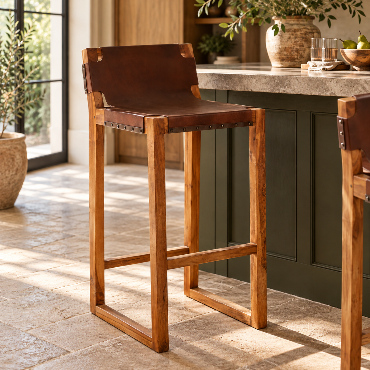 Jakarta Brown Leather Bar Chairs with teak wood frames at a kitchen island with a stone worktop, on a sunlit flagstone floor.