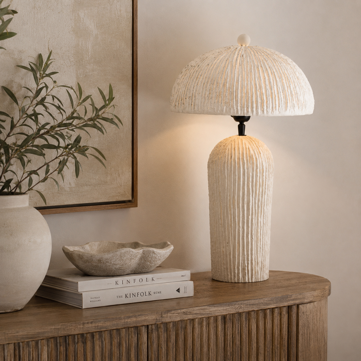 A textured cream table lamp with a ribbed cylindrical base and a matching ribbed dome shade, shown lit on a wooden console table in a styled interior setting.