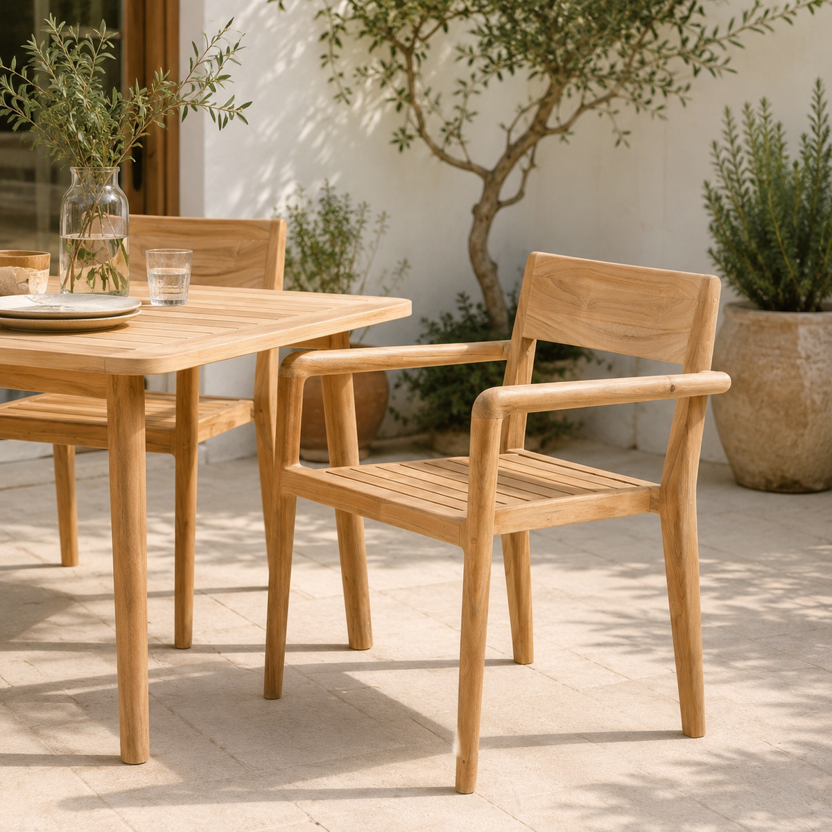 Teak wood outdoor armchair with arms beside the Shoreditch teak outdoor dining table on a patio with plants