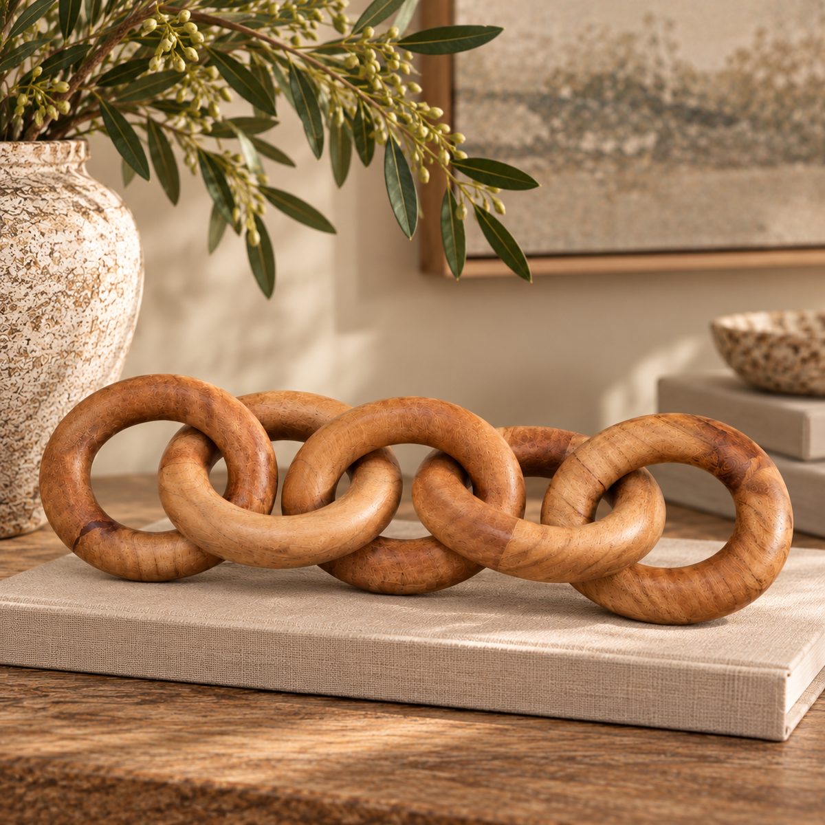 Silva Natural Wood 5 Link Chain Decor resting on a linen-covered book on a wooden console, beside a stoneware vase of olive branches