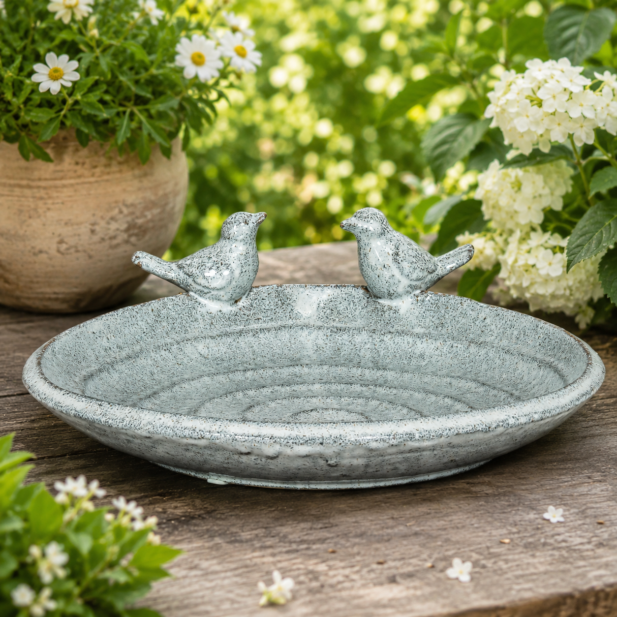 Decorative stone bird bath with two birds on a wooden surface surrounded by flowers