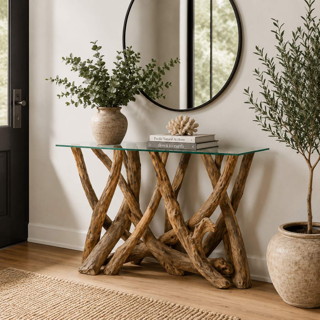 Glass console table with teak tree root base in a hallway with plants and a mirror.