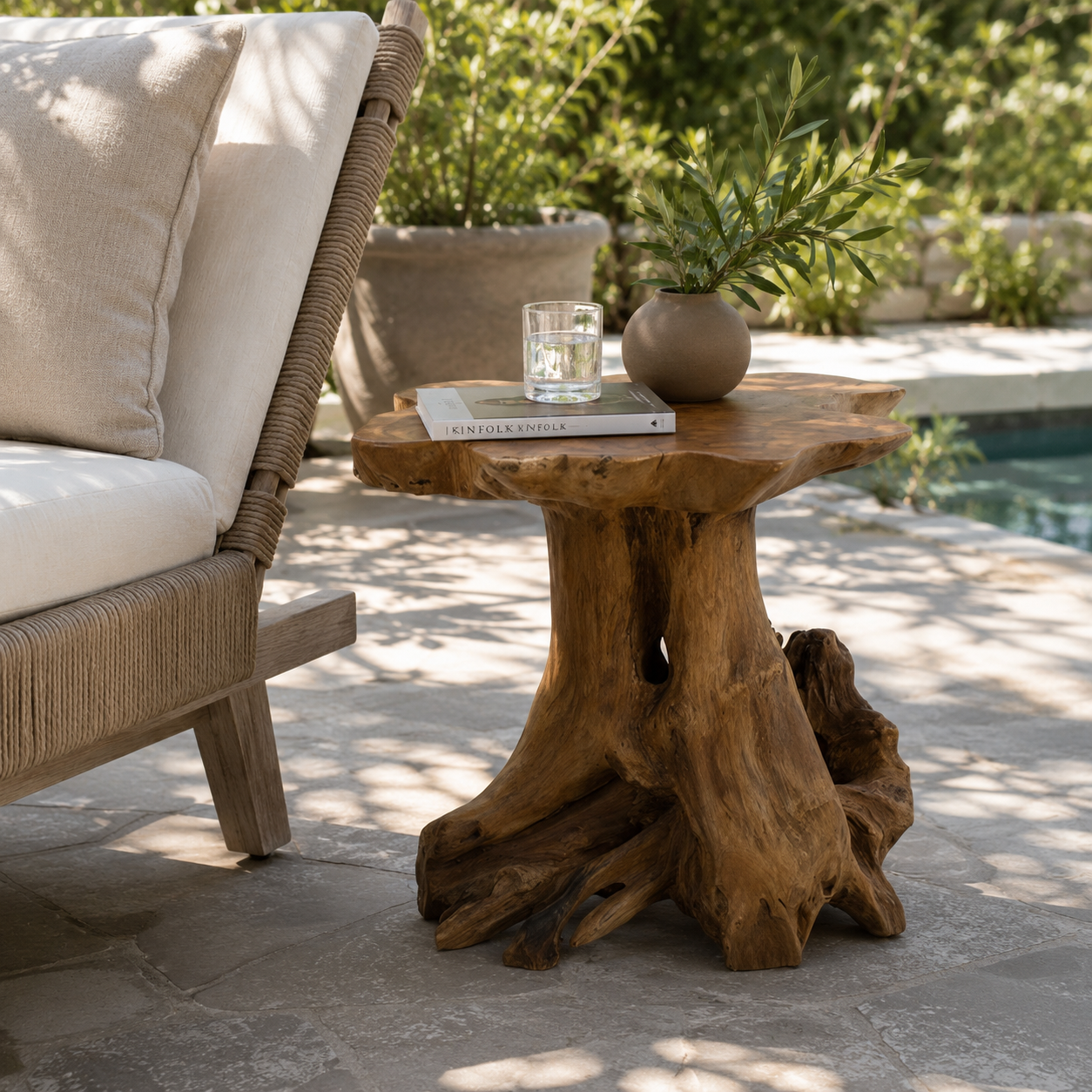 A rustic live-edge wood side table with a natural root-like base, styled in an outdoor patio setting next to a wicker chair with cream cushions.