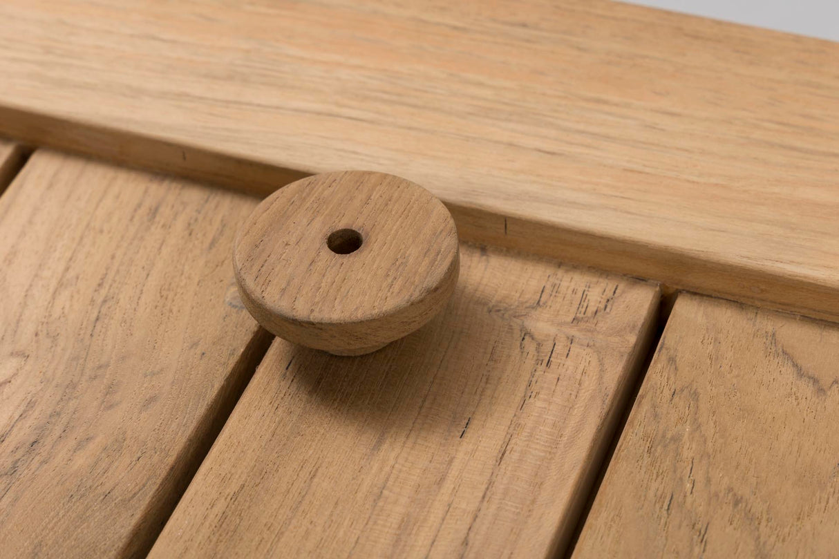 A close-up of a round wooden knob with a central hole, resting on a light oak wood slatted surface.