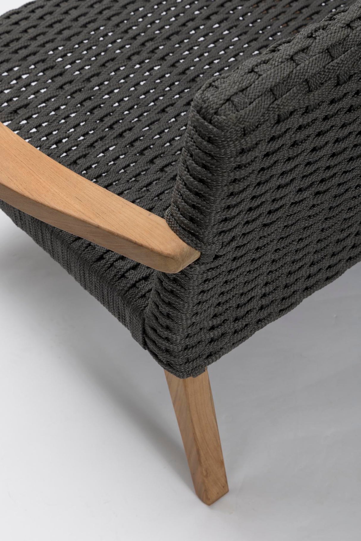 Close-up of a woven outdoor sofa with a dark grey rope seat and back, a light natural wood armrest, and a light wood leg on a white studio background.