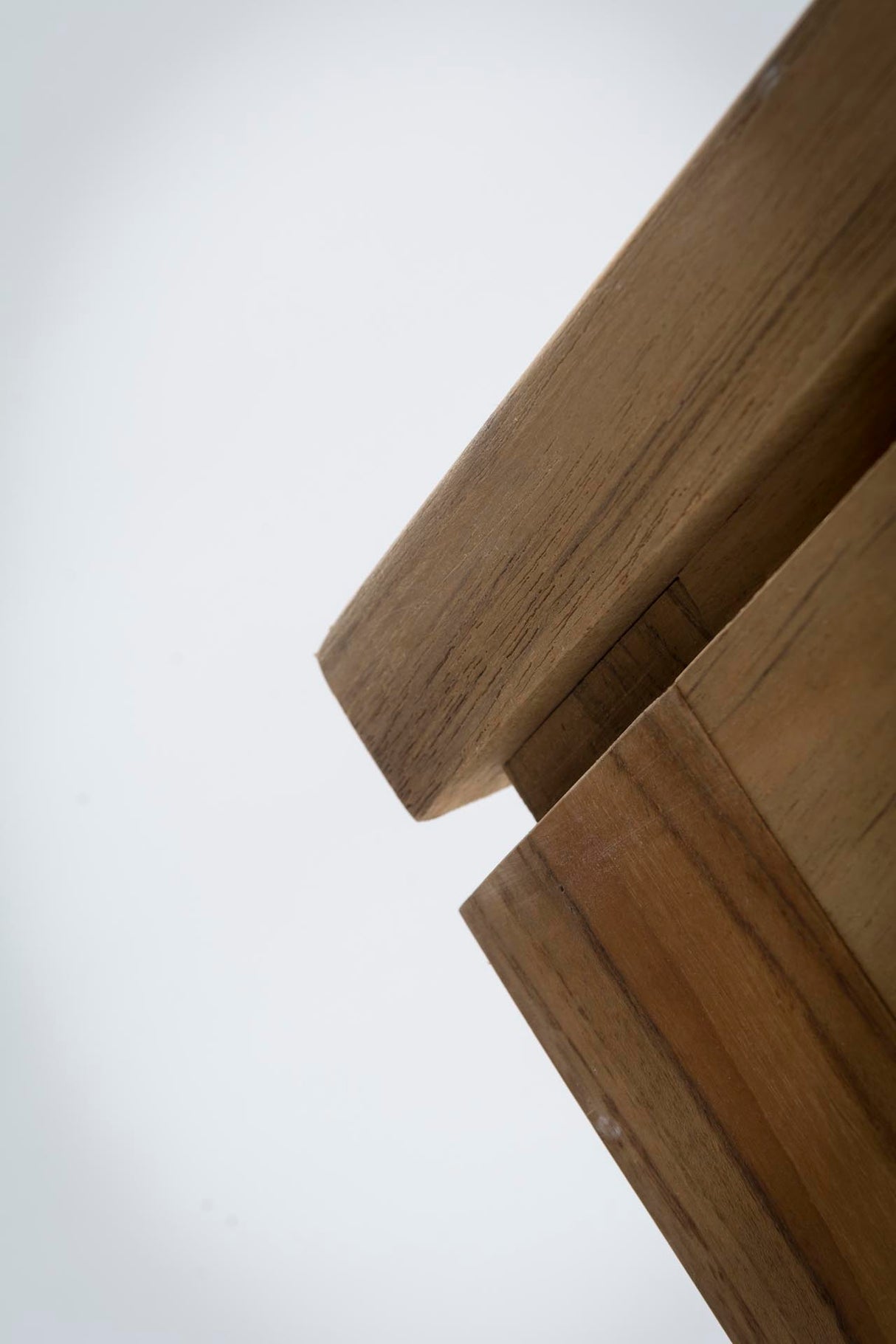 Close-up of a wooden table corner with visible grain and a light grey background.