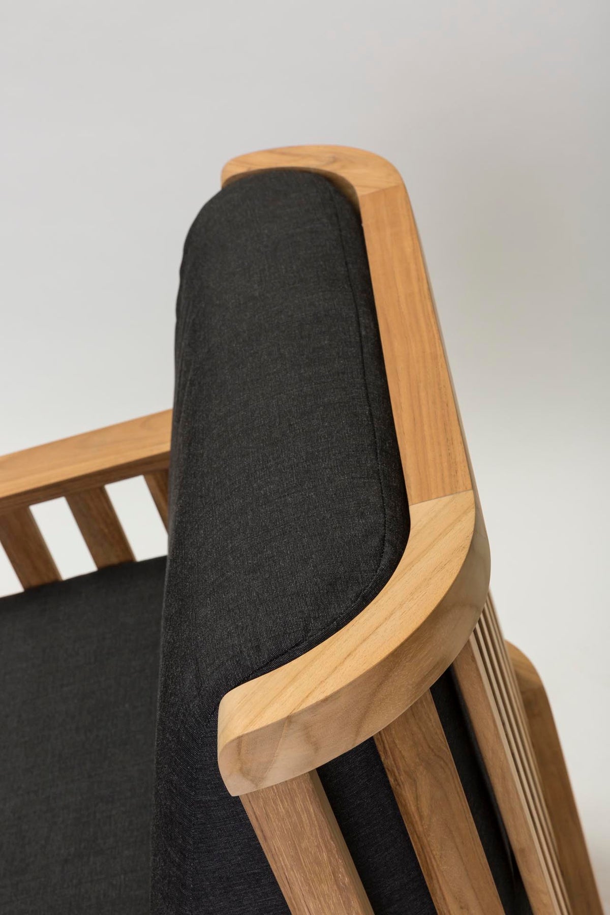 Close-up of a wooden armchair showing the backrest cushion and side frame in light natural wood with dark charcoal gray fabric upholstery.