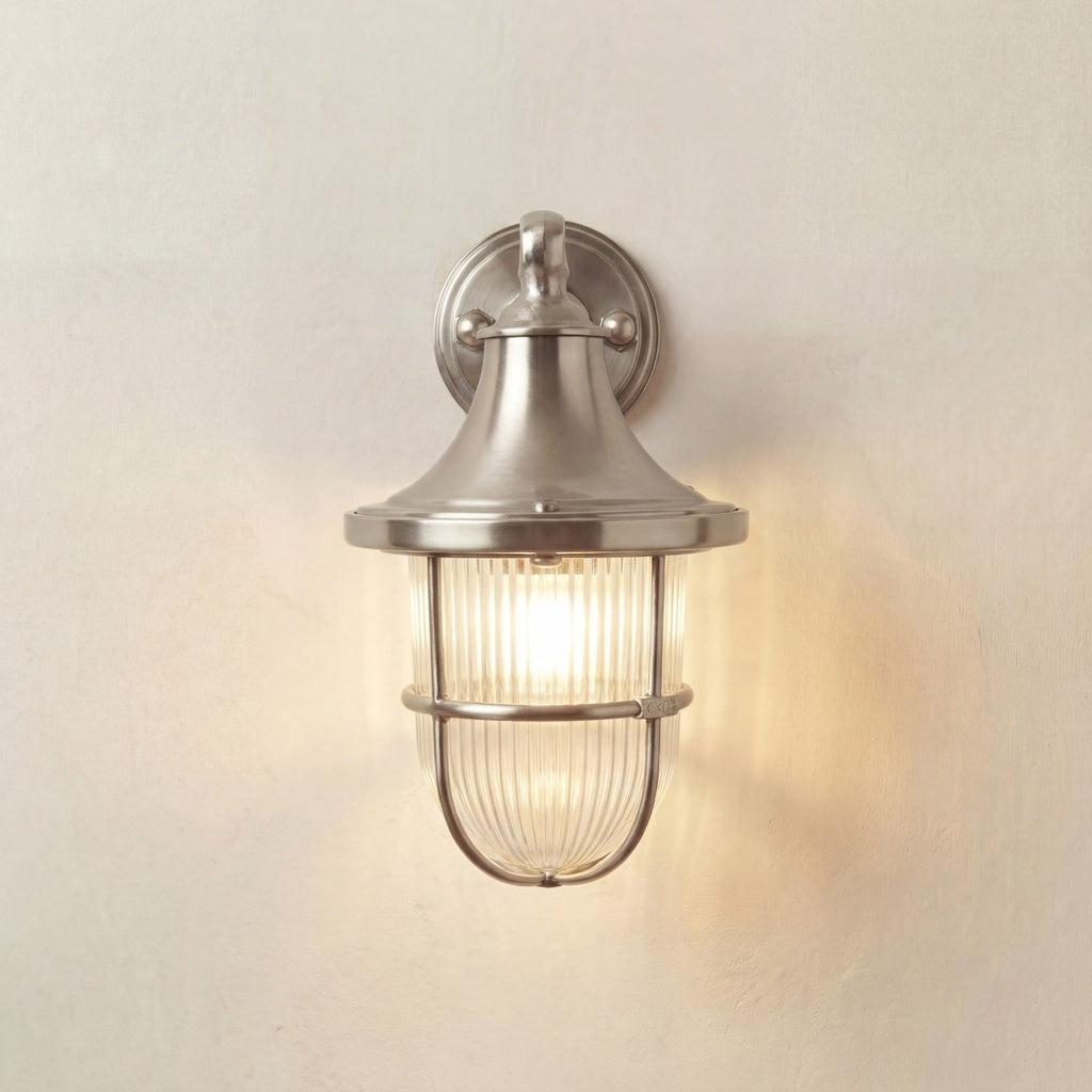 Wall-mounted outdoor light fixture with glass shade on a neutral wall.