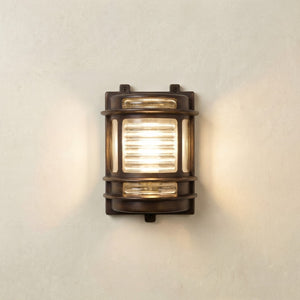 Wall-mounted outdoor light fixture with glass cover on a neutral wall.