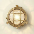 Round metallic wall light fixture with grid design on a white wall.