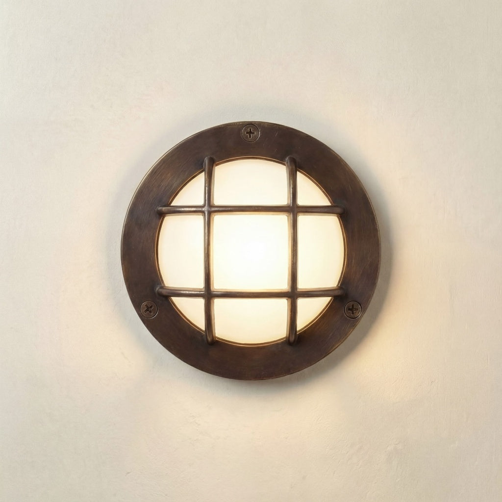 A round wall-mounted light fixture with a dark bronze metal frame and a glowing warm white glass center, mounted on a textured off-white wall.