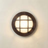 A round wall-mounted light fixture with a dark bronze metal frame and a glowing warm white glass center, mounted on a textured off-white wall.