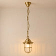 A hanging pendant light fixture with a warm brass finish, featuring a ribbed glass shade and a safety cage, suspended by a chain against a plain wall.