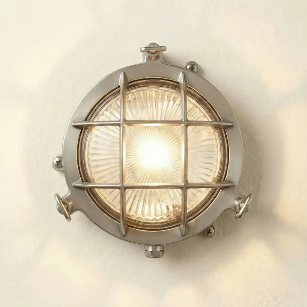 Round metallic wall light fixture with grid design on a white wall.