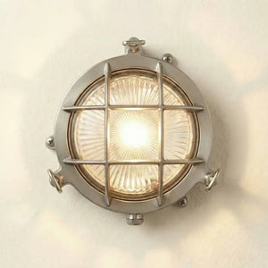 Round metallic wall light fixture with grid design on a white wall.