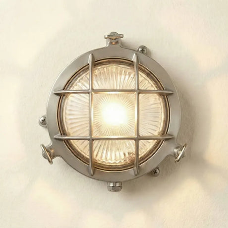 Round metallic wall light fixture with grid design on a white wall.