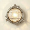 Round metallic wall light fixture with grid design on a white wall.