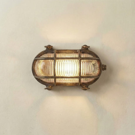 A vintage-style nautical wall sconce with a bronze-finished metal frame and ribbed clear glass panels, illuminated against a plain off-white wall.