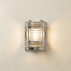 A rectangular wall-mounted light fixture with a polished chrome frame and a warm glowing light inside, mounted on a textured off-white wall.