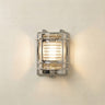 A rectangular wall-mounted light fixture with a polished chrome frame and a warm glowing light inside, mounted on a textured off-white wall.