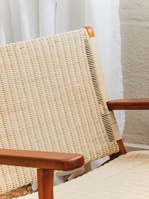 Close-up of a wicker chair with wooden armrests against a neutral background