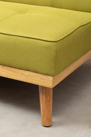 Close up of a lime green fabric sofa bed with wooden legs on a neutral floor