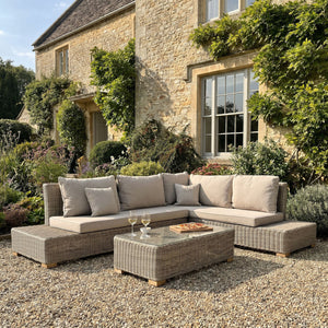 Capri outdoor large corner and coffee table set with a sectional sofa and coffee table in front of a stone building.