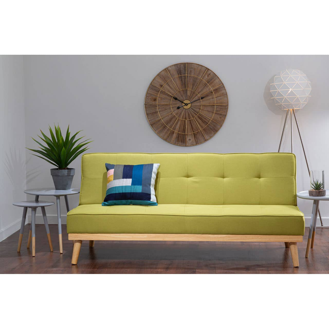 Green sofa bed with a pillow in a room with a clock on the wall and plants.