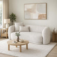 Modern living room with a light grey sofa, round wooden coffee table, and abstract art on the wall.