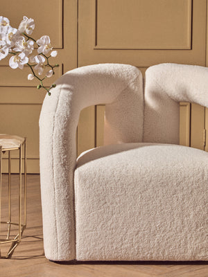 Beige textured chair with a gold side table and white flowers against a beige wall.