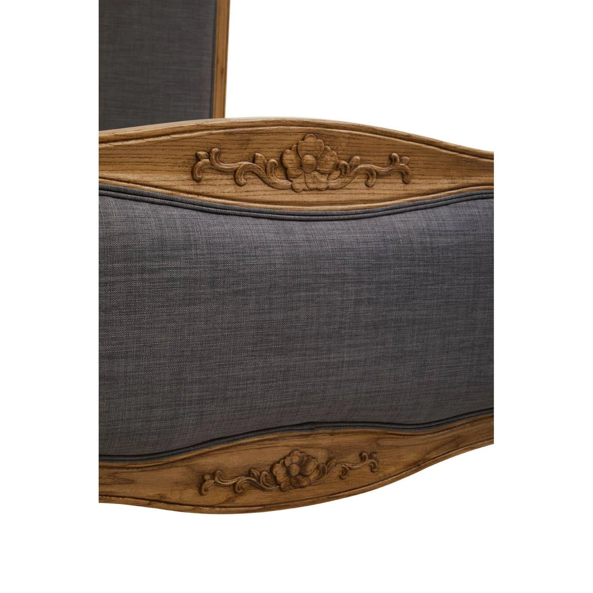 Close-up of the hand-carved floral detail on the oak frame of the Vienne bed footboard, above the grey linen-look fabric.