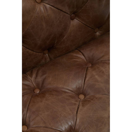 Close-up of a brown leather tufted armchair with button details.