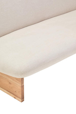 Close up of a cream linen armless sofa with wooden legs on a white background