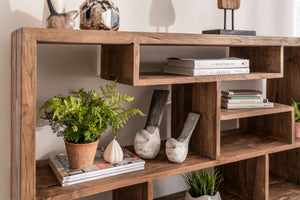 A rustic wooden open shelving unit with multiple cubby compartments, styled with books, potted ferns, ceramic vases, and decorative objects against a neutral wall.