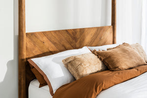 Close view of the Ashcombe four poster's chevron-laid reclaimed teak headboard behind rust and cream bedding.
