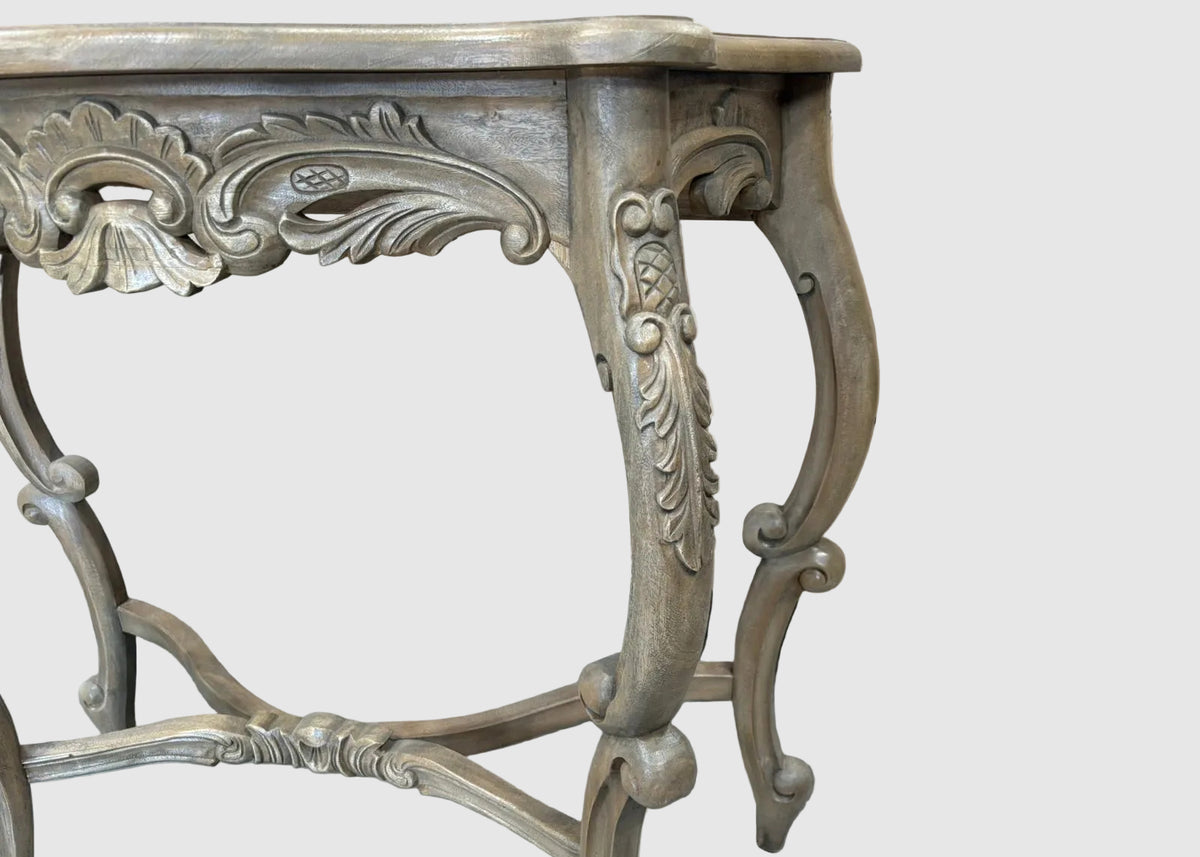 An ornate carved console table with a distressed gray and silver finish, shown against a plain light gray background.