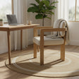 Wooden chair with beige cushion next to a wooden desk with a laptop and cup, in a bright room with curtains and a plant.