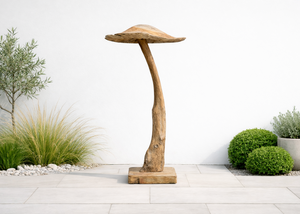 Wooden mushroom-shaped ornament in a garden setting with plants and a white wall.