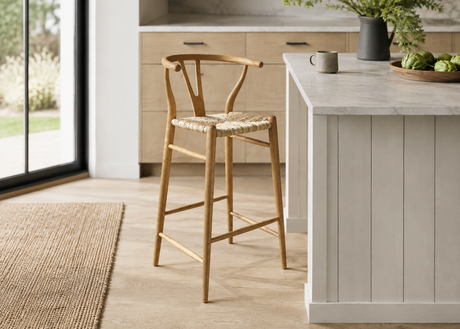 A light natural wood bar stool with a woven seat sits beside a white kitchen island in a bright, modern kitchen.