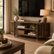 A round wooden TV stand with vertical slat detailing, styled in a cozy living room setting with a television, lamps, books, and plants.