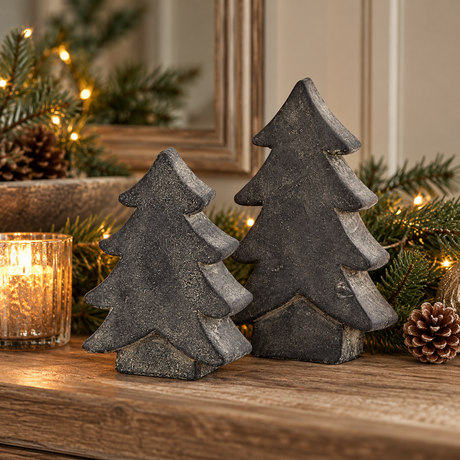 Two charcoal grey Amalfi trees on a wooden mantel with a lit candle, pine sprigs, pinecones and fairy lights